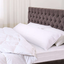 White body pillow with two long sides, placed on a bed against a tufted headboard.