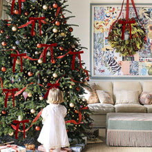 Red velvet Christmas bows on a decorated Christmas tree with ornaments and garlands.
