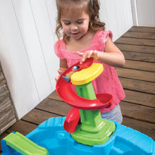 Toddler playing with a blue water table using red and green water-play parts