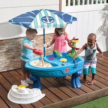 Kids playing at a blue water table with umbrella and colorful splash tools