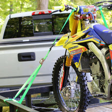 Green tie-down strap set with cam buckles and hooks securing a dirt bike