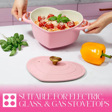 Pink heart-shaped Dutch oven with handles, filled dish visible, heart lid placed nearby