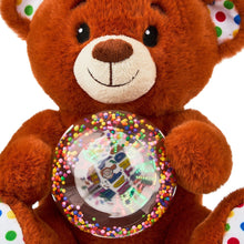 Tan bear plush close-up with smiling face and glowing music globe on belly.