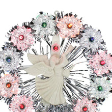 Cream angel figure in center of silver tinsel wreath with multi-color lights