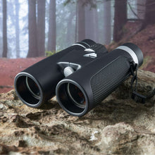 Black binoculars resting on rocks, two eyepieces with textured side grip