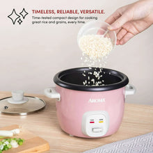 Pink rice cooker with black inner pot and rice grains being poured into the opening