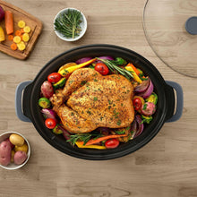 Black oval stoneware slow cooker insert with handles, filled with cooked chicken and vegetables