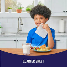 Child holding a quarter sheet paper towel at a kitchen table.