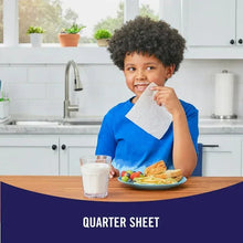 Child holding a white square paper towel at a kitchen table