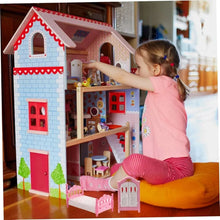 Child playing with a wooden dollhouse and pink miniature furniture accessories.