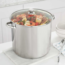Stainless steel stock pot with glass lid and side handles, filled with food