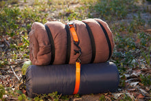 Orange cam buckle tie-down strap securing a rolled pad outdoors