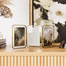 Three-panel gold metal folding picture frame showing landscape photos in open frames