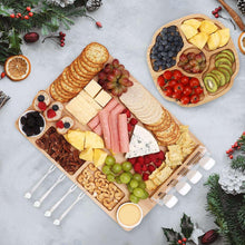 Bamboo charcuterie board with white-handled knives and round snack tray for fruit and cheese