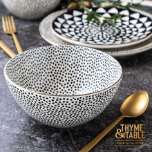 Ceramic soup bowl with black dot speckle pattern and gold rim on tabletop