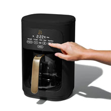 Black programmable drip coffee maker with hand pressing touch controls.