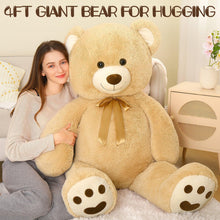 Giant tan teddy bear plush with gold neck ribbon and oversized paw pads