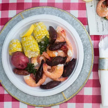 White dinner plate filled with shrimp, sausage, corn, and herbs