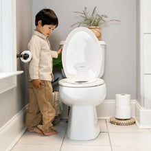 Toddler using a flip-up potty seat on a white toilet in a bathroom