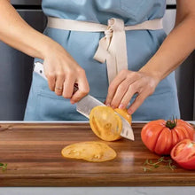 Stainless steel chef knife cutting a yellow onion on a wooden board
