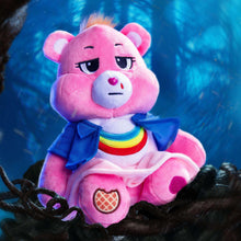 Pink plush bear with blue jacket and rainbow collar on dark fabric base