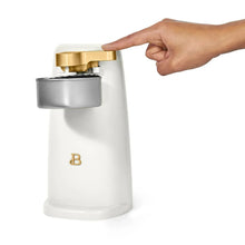 White electric can opener lifting a can lid with a hand