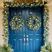 Pre-lit Christmas garland set with dark green branches, metallic baubles, warm lights on doorway