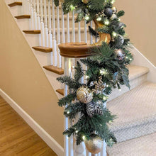 Pre-lit artificial Christmas garland with dark green branches, metallic baubles, warm lights