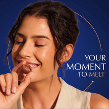 Woman holding a dark chocolate truffle, smiling with a bite
