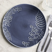Blue stoneware dinner plate with floral vine and fern design, shown with utensils