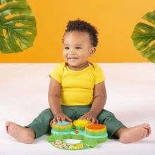 Baby playing a green musical drum toy with three colored drum pads and jungle graphics