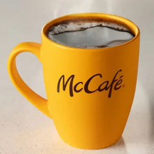 Yellow ceramic coffee mug filled with dark coffee with McCafe logo