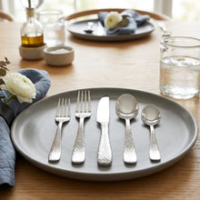 Hammered stainless steel flatware arranged on a plate, showing forks, knife, and spoons