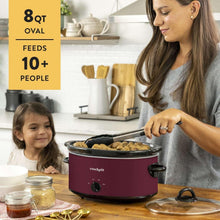 Maroon oval slow cooker with black lid and front dial, used at the kitchen table