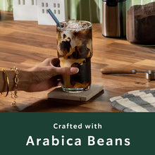 Iced coffee glass with hand on coaster; crafted with Arabica beans text