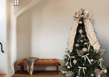 Decorated Christmas tree with champagne baubles, large bows, and ribbon streamers on green branches.