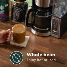 Whole bean coffee setup with glass mug, coffee maker, and coffee bag on counter