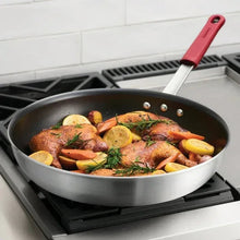 Nonstick fry pan with browned meat, lemon slices, and herbs on stovetop
