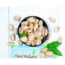 Roasted salted pistachios in a black bowl with scattered pistachio shells