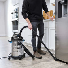 Stainless steel wet/dry vacuum with black canister and long hose attachment by wall