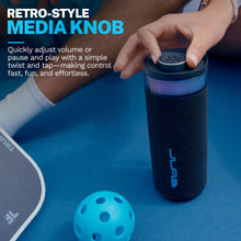 Portable speaker with top media knob and textured body, blue accent logo on front.