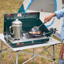 2-burner propane stove on table with kettle and frying pan, dark green
