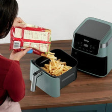 Sage air fryer with pull-out basket loaded with fries, being filled by hands.