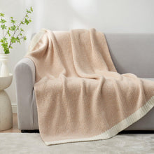 Beige throw blanket with knit texture, draped over sofa and trimmed with a cream edge.
