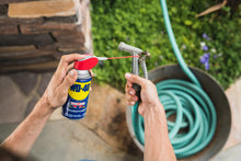 WD-40 spray can with red straw nozzle in hands applying to a garden faucet