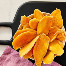 Unsweetened dried mango slices in a black scoop, golden orange pieces
