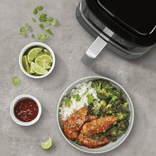 Black air fryer basket with handle, with bowls of cooked food nearby