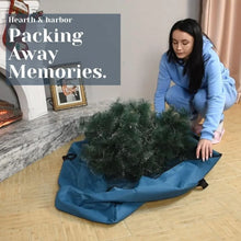 Christmas tree storage bag laid open on the floor with a person folding a tree inside
