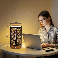Table lamp with black cylindrical branch-pattern shade and wooden base on a desk.