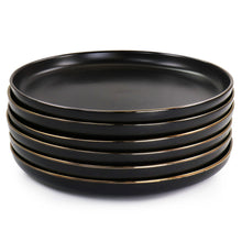 Stack of black stoneware dinner plates with gold rims, shallow angle